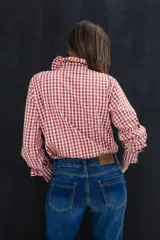 Camisa de algodón con estampado de cuadros en rojo y blanco, con detalles de bordado vertical. Presenta volados románticos en la parte frontal, cuello y puños, con un corte clásico y holgado.