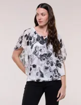 Blusa de gasa semitransparente con hilos de lúrex, diseño estampado floral en tonos blanco, gris y negro, silueta holgada tipo capa y escote redondo con detalle metálico.