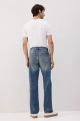 Jeans de cinco bolsillos en denim de algodón rígido, color azul medio con efecto desgastado y lavado. Modelo de cintura clásica con cierre de botón y corte relajado de cadera a bajo con pierna recta más amplia.