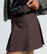 Short pollera de estilo sastre en color marrón, con diseño de pliegues frontales y cierre lateral. Incluye un cinturón desmontable de cuero sintético con hebilla metálica.