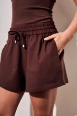 Short verde militar de lino y poliéster, de tiro medio con cintura elástica fruncida y cordón ajustable delantero. Cuenta con bolsillos laterales.