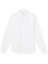 Camisa blanca de manga larga con cuello clásico y botones frontales. Presenta un pequeño bolsillo en el pecho con el logo de Calvin Klein Jeans bordado en tono gris claro.