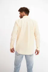 Camisa de hombre color crema, de corte clásico, con cuello abotonado y mangas largas.