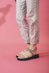 Sandalias de plataforma con tiras cruzadas en el empeine y ajuste de velcro en el tobillo. Presentan una combinación de colores beige y marrón, con suela de goma negra.