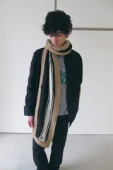 Bufanda tejida a rayas en tonos beige, negro y blanco, con terminaciones tejidas a crochet y etiqueta de marca en el extremo.