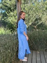 Vestido camisero largo de lino blanco, con cuello camisero, manga corta enrollada y cierre frontal de botones de nácar. Presenta aberturas laterales en el bajo.