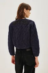 Campera corta acolchada color azul marino con cierre frontal y bordados florales en negro con cuentas y lentejuelas en el pecho y parte superior.