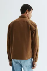 Sobrecamisa de lona gruesa de algodón color marrón, con cuello, tapeta de botones a presión y canesú en la espalda. Mangas largas con botón a presión en los puños y dos bolsillos superiores de parche. Bajo levemente redondeado. Corte oversized.