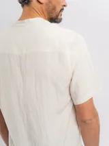 Camisa de manga corta color beige, con cuello mao, bolsillo ojal en el pecho y cierre frontal parcial con botones.