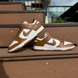 Championes Nike Dunk Low con diseño bicolor en blanco y marrón. Presentan una silueta clásica de perfil bajo con paneles de cuero, cierre de cordones y suela de goma resistente.