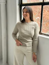 Sweater de punto color visón con diseño de trenzas verticales, cuello redondo y mangas largas.