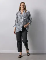 Camisa estampada con hojas en tonos celeste, naranja y verde. Tiene cuello con solapa, abertura central con botones, bolsillos aplicados en la parte delantera y mangas 3/4 con lazo.