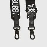Correa para cartera de poliéster en color negro con el logo de la marca estampado en blanco de forma repetida. Cuenta con detalles en cuero vegano en los extremos y ganchos metálicos tipo mosquetón para intercambiar fácilmente.