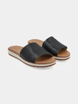 Sandalia de mujer con tira ancha de cuero sintético texturizado color negro. Suela marrón con plataforma blanca y base marrón.