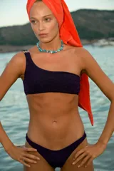 Bikini de tela lúrex color violeta con acabado brillante. El corpiño es tipo top de un solo hombro con hebilla metálica decorativa en el tirante. La bombacha es de corte vedetina.