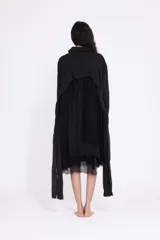 Vestido camisero negro de largo midi, con diseño asimétrico y efecto de capas. Presenta cuello clásico, cierre frontal de botones y mangas largas con puño. El bajo es irregular y deshilachado.