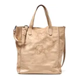 Cartera tipo tote bag de gamuza en color tostado, con doble asa de mano y correa ajustable extraíble. Presenta detalles de tachas metálicas en los laterales y un logo circular grabado en el centro.