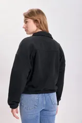Campera de polar negro con cierre frontal, cuello alto, bolsillos laterales y corte holgado.