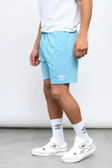 Bermuda deportiva Umbro de color celeste, con cintura elástica con cordón ajustable y el logo de la marca bordado en blanco en la parte inferior de la pierna izquierda.