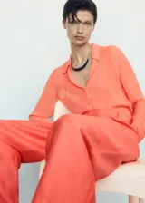 Pantalon de corte wideleg color naranja, confeccionado en mezcla de lino y lyocell. Presenta diseño de tiro alto con trabillas para cinturón, pinzas frontales, dos bolsillos laterales y dos bolsillos de ribete en la parte posterior. Cierre oculto de botón, gancho y cremallera.