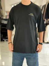 Remera oversize color beige, con mangas cortas y cuello redondo. Presenta un estampado tipográfico en la espalda con la frase "There are no facts, only interpretations" y otros detalles de diseño.