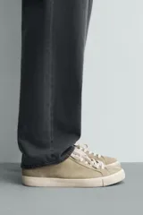 Zapatilla de cordones para hombre, fabricada en piel con acabado serraje (gamuza) color beige claro. Presenta detalles de pespuntes y una suela gruesa de goma a contraste en color crema.
