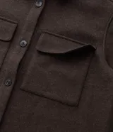 Camisa de corte largo tipo shacket, confeccionada en polivelour color marrón. Presenta cuello camisero, cierre frontal con botones, hombros caídos, mangas largas y dos bolsillos frontales aplicados con solapa.