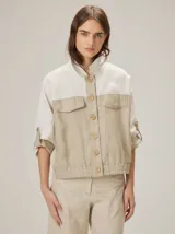 Chaquetas de lino bicolor en tonos blanco y beige, con diseño holgado, cuello alto, cierre frontal de botones, bolsillos con solapa en el pecho y mangas cortas con presilla y botón.