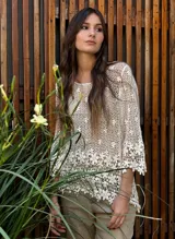 Top de tejido de punto crochet color beige claro, con manga tres cuartos y escote redondo. Presenta un patrón de flores caladas y terminación festoneada en el ruedo.