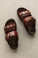 Sandalias bajas de cuero color marrón con doble tira, una con textura de piel de serpiente y hebilla lateral, y otra con apliques de tachas redondas color cobre.