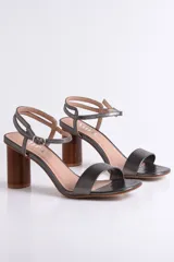 Sandalia de cuero color peltre, con tira ancha sobre los dedos y tira fina con hebilla al tobillo. El taco es cilíndrico de madera clara.