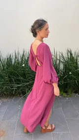 Vestido largo color bordó con escote en V profundo, detalle de nudo central y aberturas laterales en la cintura. Presenta mangas largas abullonadas con puños elásticos y falda con tajo frontal pronunciado.