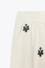 Pantalón color crema de tiro medio con cintura elástica ajustable y bolsillos delanteros. Presenta bordados florales en negro y corte ancho.