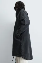 Abrigo de corte relajado confeccionado en denim de algodón con efecto lavado. Presenta cuello subido, cierre frontal con cremallera oculta por solapa con botones a presión, bolsillos de vivo en el pecho y de solapa en la cadera. Incluye mangas largas con puños ajustables y bajo con cordón regulable.