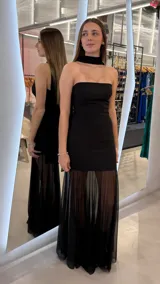 Vestido largo negro strapless con escote palabra de honor, diseño ajustado en el cuerpo y falda larga semitransparente con detalles plisados. Incluye una pieza al cuello tipo choker unida a la parte posterior del vestido.
