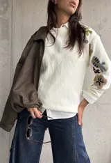 Sweater de punto color natural con cuello redondo y mangas largas, decorado con bordados florales multicolores en las mangas y hombros.