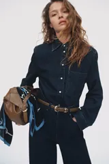 Camisa en denim de algodón con hombreras, cuello clásico, botones a presión nacarados, bolsillo frontal aplicado y bajo redondeado.