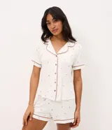 Pijama corto de dos piezas confeccionado en viscolycra blanca con estampado floral y vivo en contraste. Incluye una camisa de manga corta con cuello solapa y cierre frontal de botones, y un short con cintura elástica.