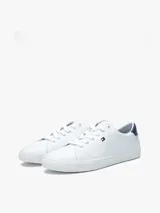 Zapatillas urbanas Tommy Hilfiger de corte bajo, color blanco con detalle azul en el talón. Tienen diseño con cordones, suela de goma blanca y pequeño logo bordado en el lateral.