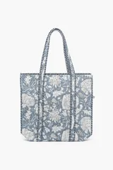 Bolso tipo tote con diseño acolchado y estampado floral en tonos azules y blancos. Presenta asas largas con detalles de costuras decorativas en contraste y bordes reforzados.
