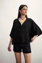 Blusa negra de corte holgado con cuello polo y cierre frontal parcial. Presenta mangas cortas amplias y un diseño minimalista.