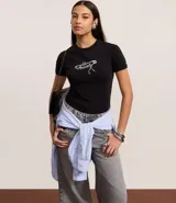 Remera negra de manga corta, corte ajustado al cuerpo, con cuello redondo y estampa frontal en blanco con la palabra "Anxiety" en tipografía cursiva y detalles gráficos.