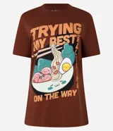 Remera marrón de algodón con cuello redondo y mangas cortas. Estampa frontal de un plato de lámen con el texto "Trying My Best Relaxing On The Way".