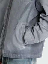 Campera de estilo urbano con efecto desgastado, confeccionada en tejido gris con acabado lavado. Presenta cuello de cuero negro en contraste, cierre frontal con cremallera y diseño de corte holgado.