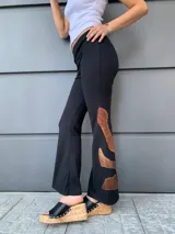 Pantalón negro de tejido de punto con corte acampanado y apliques de cuero sintético color cobre en la parte inferior de las piernas.