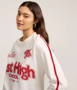 Buzo de tejido de punto color blanco hueso, con cuello redondo y mangas largas. Presenta un estampado frontal en rojo con el texto "East High School EST. 2006", el logo de los Wildcats y la inscripción "GO WILDCATS". Las mangas tienen una franja lateral roja.