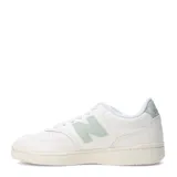 Championes urbanos New Balance, modelo Pop N Pack Leather, de color blanco con detalles en verde pastel en el logo lateral y la suela. Presentan una silueta clásica de corte bajo con perforaciones en la puntera y cierre de cordones.