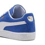 Championes Puma modelo Suede Classic, confeccionados en gamuza de color negro con la icónica franja lateral en blanco y el logotipo de la marca impreso en dorado metalizado en el lateral. Suela de goma texturizada en color blanco.