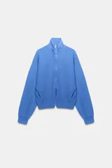Chaqueta azul de algodón con cuello alto, cierre frontal de cremallera, bolsillos laterales y mangas largas con puños elásticos.