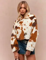 Chaqueta corta de textura tipo peluche con estampado animal print estilo vaca en tonos blanco y marrón. Presenta cuello alto, cierre frontal y corte oversize.